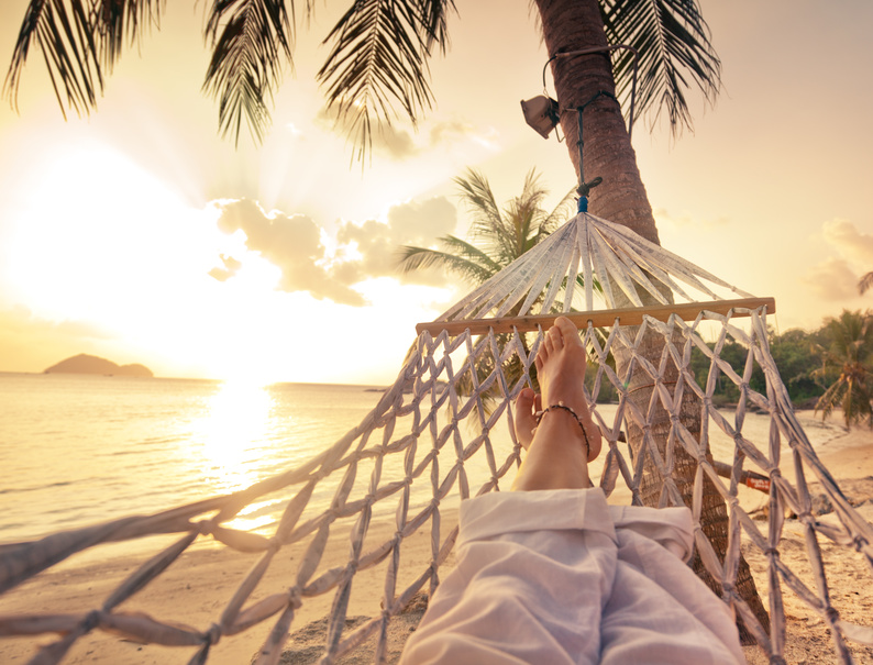 Female legs in a hammock on a background of the sea, palm trees and sunset. Vacation concept